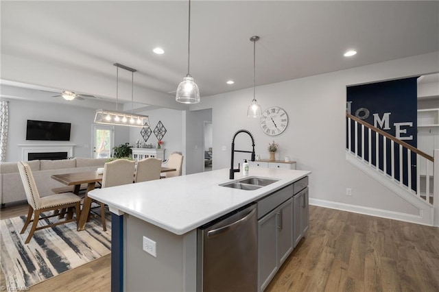 kitchen featuring stainless steel dishwasher, wood-type flooring, ceiling fan, sink, and a kitchen island with sink