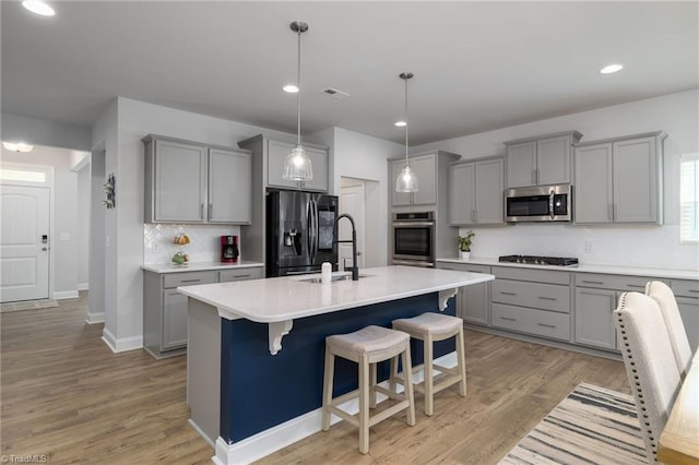 kitchen featuring stainless steel appliances, light hardwood / wood-style flooring, a kitchen island with sink, and gray cabinetry