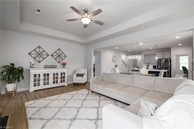 living area featuring baseboards, a tray ceiling, visible vents, and wood finished floors