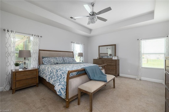 bedroom with light colored carpet, multiple windows, and a tray ceiling