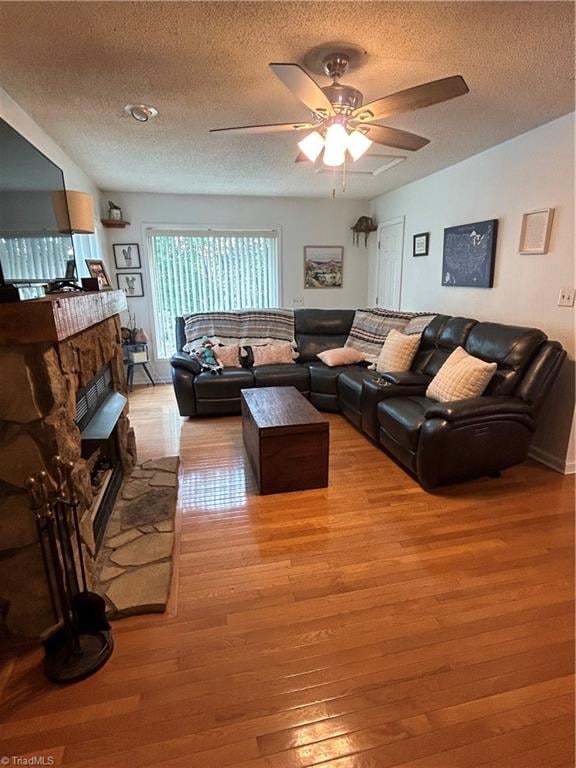 living room featuring a fireplace, ceiling fan, light hardwood / wood-style floors, and a textured ceiling