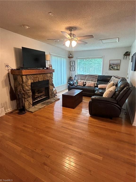 living room with wood-type flooring, a stone fireplace, a textured ceiling, and ceiling fan