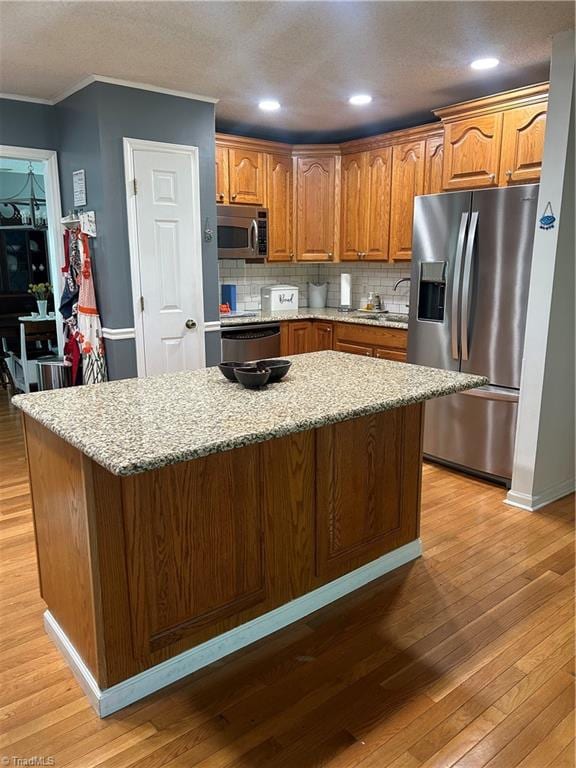 kitchen with light stone counters, appliances with stainless steel finishes, decorative backsplash, and light hardwood / wood-style flooring