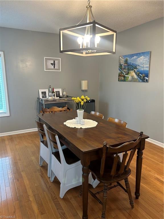 dining space with wood-type flooring, a notable chandelier, and a textured ceiling