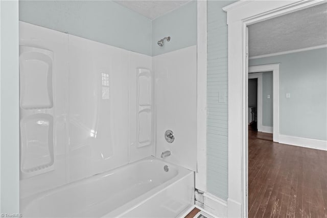 full bathroom with a textured ceiling, wood finished floors, baseboards, ornamental molding, and washtub / shower combination