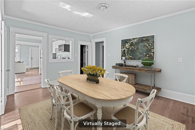 dining room with ornamental molding, a textured ceiling, baseboards, and wood finished floors