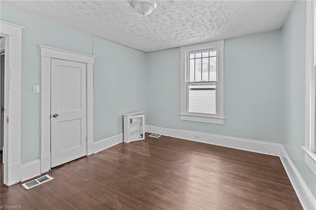 spare room with dark wood-style floors, a textured ceiling, visible vents, and baseboards