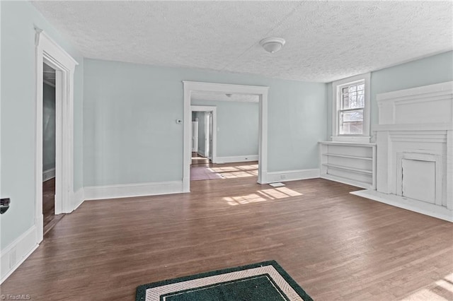 unfurnished living room with a textured ceiling, baseboards, and wood finished floors