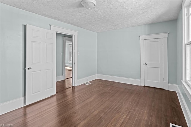 unfurnished room featuring dark wood-style floors, visible vents, a textured ceiling, and baseboards