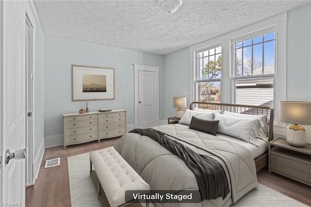 bedroom with visible vents, a textured ceiling, baseboards, and wood finished floors