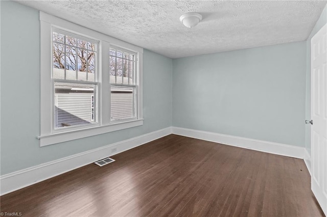 spare room with dark wood-style floors, visible vents, a textured ceiling, and baseboards