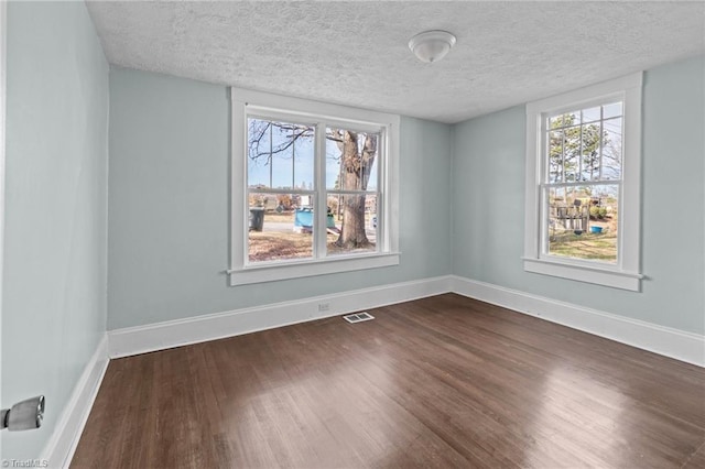 spare room featuring dark wood-style flooring, visible vents, a textured ceiling, and baseboards