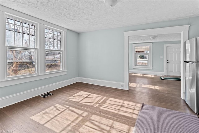 spare room featuring a textured ceiling, wood finished floors, visible vents, and baseboards