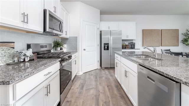 kitchen with stainless steel appliances, white cabinets, stone countertops, and sink