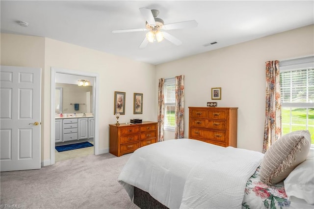 bedroom with visible vents, baseboards, ensuite bathroom, light colored carpet, and a ceiling fan
