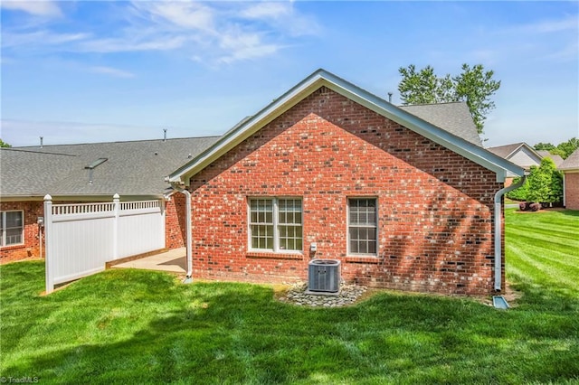 rear view of house featuring a lawn, central AC unit, fence, and brick siding