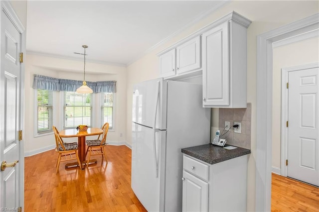 kitchen featuring white cabinets, dark countertops, freestanding refrigerator, light wood-type flooring, and ornamental molding
