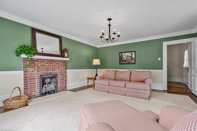 living room featuring ornamental molding, a wainscoted wall, a chandelier, wood finished floors, and a brick fireplace