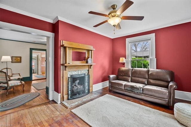 living room with ceiling fan, a fireplace, ornamental molding, baseboards, and hardwood / wood-style flooring