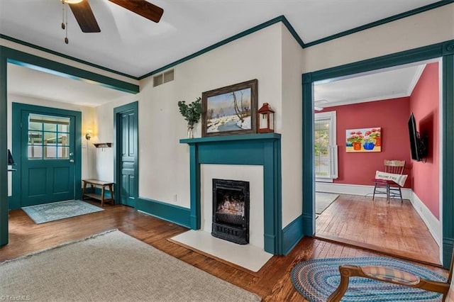 foyer entrance featuring visible vents, a ceiling fan, ornamental molding, and wood finished floors