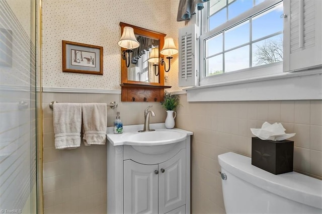 full bathroom featuring toilet, vanity, wallpapered walls, and a wainscoted wall