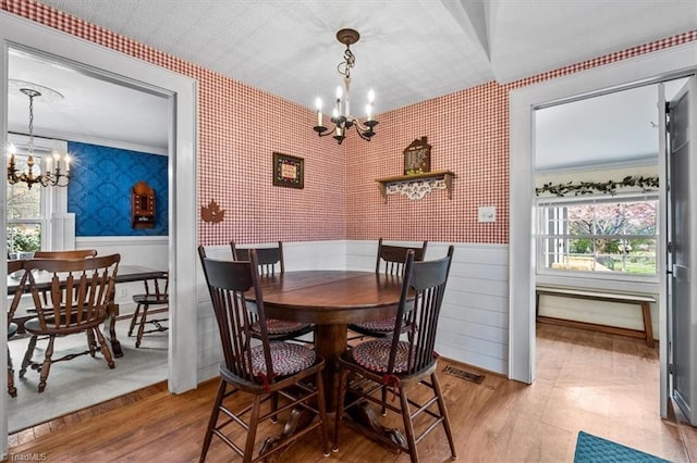 dining room featuring a chandelier, wainscoting, visible vents, and wallpapered walls
