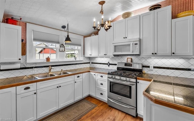 kitchen featuring white microwave, gas stove, a sink, decorative light fixtures, and light wood finished floors