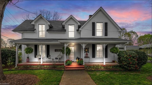 view of front of property with a porch, a shingled roof, and a lawn