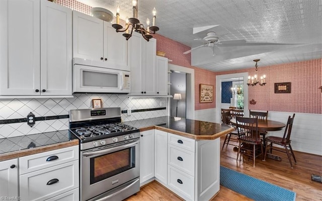 kitchen featuring white microwave, light wood finished floors, stainless steel gas stove, and a peninsula