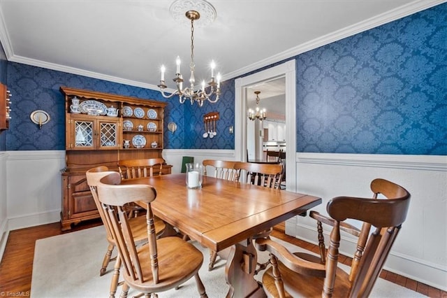 dining room with crown molding, a wainscoted wall, a chandelier, wood finished floors, and wallpapered walls