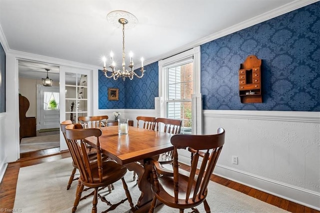 dining area featuring a chandelier, crown molding, wood finished floors, wallpapered walls, and a wainscoted wall