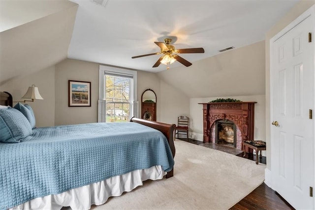 bedroom featuring dark wood-style flooring, vaulted ceiling, a fireplace, visible vents, and ceiling fan