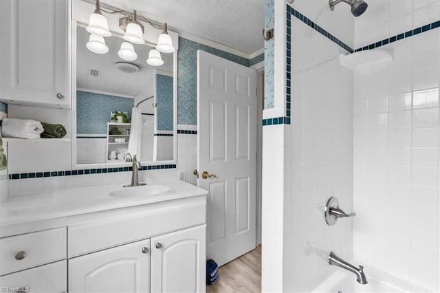 bathroom featuring vanity, wallpapered walls,  shower combination, a textured ceiling, and tile walls