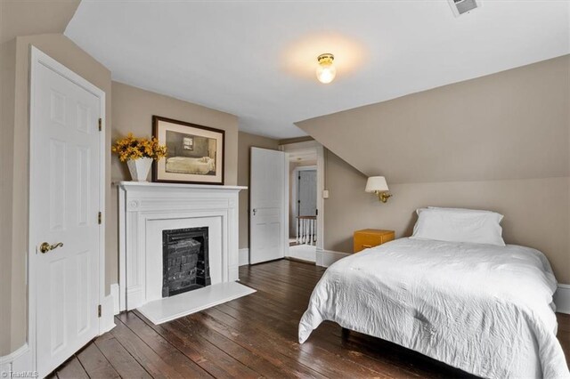 bedroom featuring baseboards, vaulted ceiling, a fireplace, visible vents, and hardwood / wood-style floors