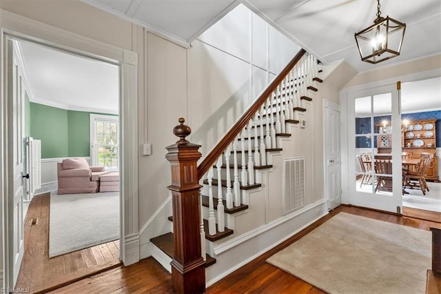 staircase featuring a decorative wall, visible vents, ornamental molding, and hardwood / wood-style floors