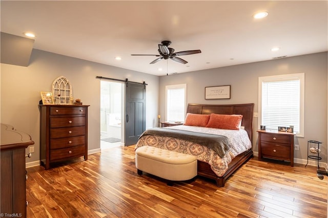 bedroom featuring ensuite bath, hardwood / wood-style floors, a barn door, and ceiling fan