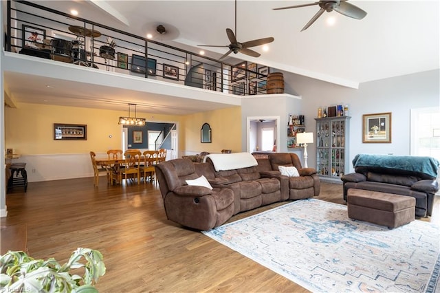 living room with high vaulted ceiling, ceiling fan with notable chandelier, and hardwood / wood-style floors