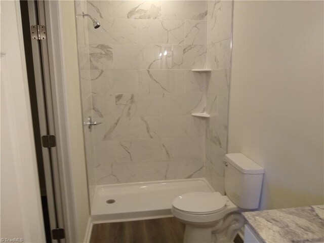 bathroom featuring toilet, hardwood / wood-style flooring, tiled shower, and vanity