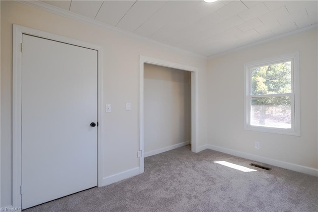 unfurnished bedroom with carpet flooring, baseboards, visible vents, and ornamental molding