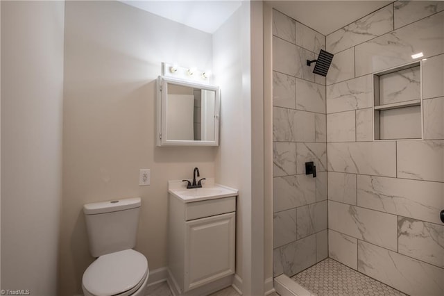 bathroom featuring vanity, toilet, baseboards, and tiled shower