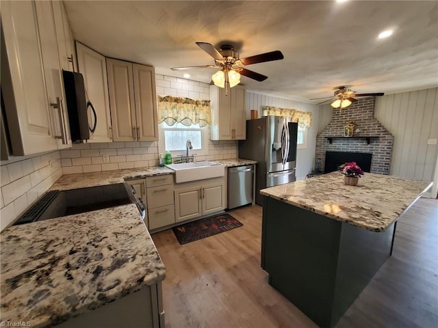 kitchen featuring a sink, stainless steel appliances, light wood-style floors, a fireplace, and decorative backsplash