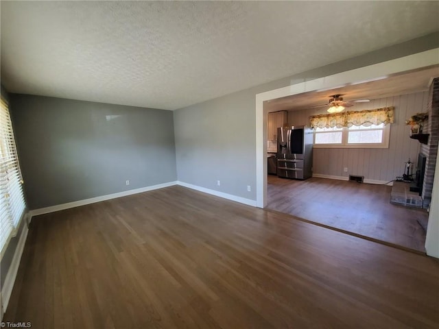 unfurnished living room with a ceiling fan, baseboards, dark wood finished floors, a fireplace, and a textured ceiling