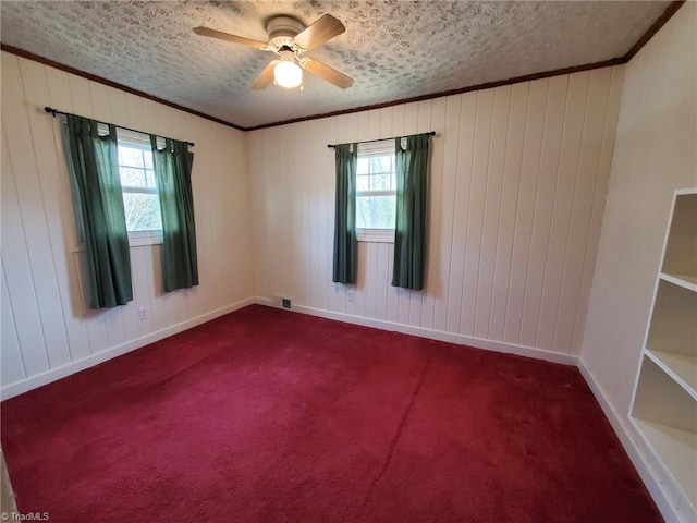 unfurnished room with a wealth of natural light, dark colored carpet, and ornamental molding