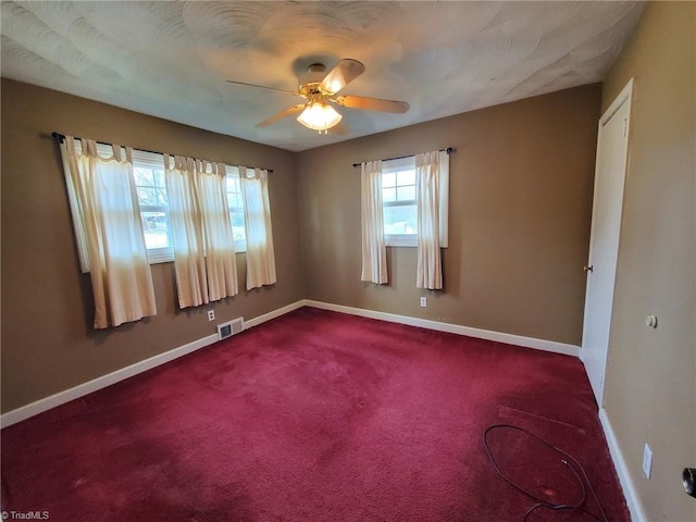 spare room featuring baseboards, visible vents, dark carpet, and ceiling fan