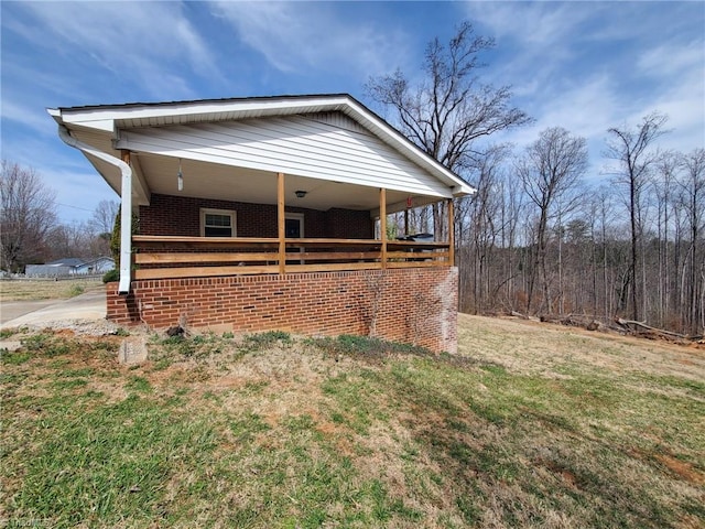 view of side of property with brick siding, covered porch, and a lawn