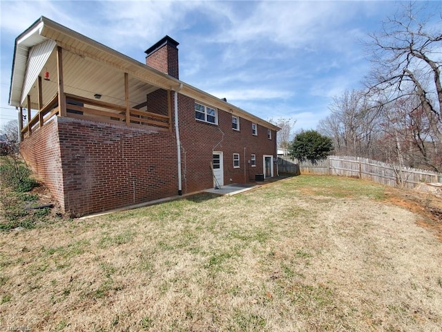 back of house featuring a patio, fence, a yard, brick siding, and a chimney