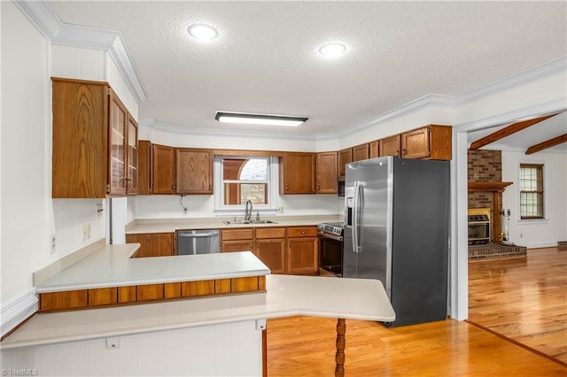 kitchen featuring light wood finished floors, a peninsula, brown cabinetry, stainless steel appliances, and a sink