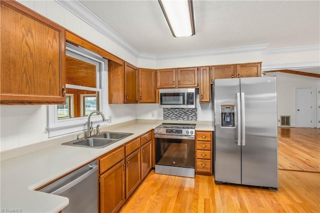 kitchen featuring brown cabinets, ornamental molding, a sink, appliances with stainless steel finishes, and light countertops