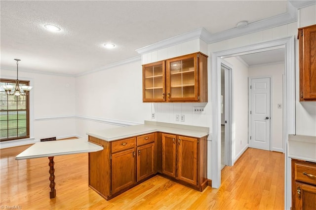 kitchen featuring a peninsula, ornamental molding, brown cabinetry, and light countertops