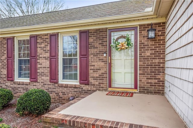 doorway to property featuring brick siding and a shingled roof